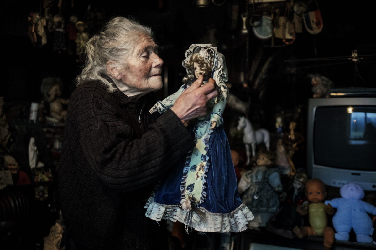 Marie-Claude joue dans son salon avec sa poupée préférée. « Elle est magnifique, n’est-ce pas ? », me dit-elle. Elle la cajole, caresse ses joues, enlève la poussière de sa robe et la remet à sa place, derrière la télé, lui ordonnant de ne pas bouger. / Extrait de « Marie-Claude, la dame aux poupées », © Mélanie Wenger