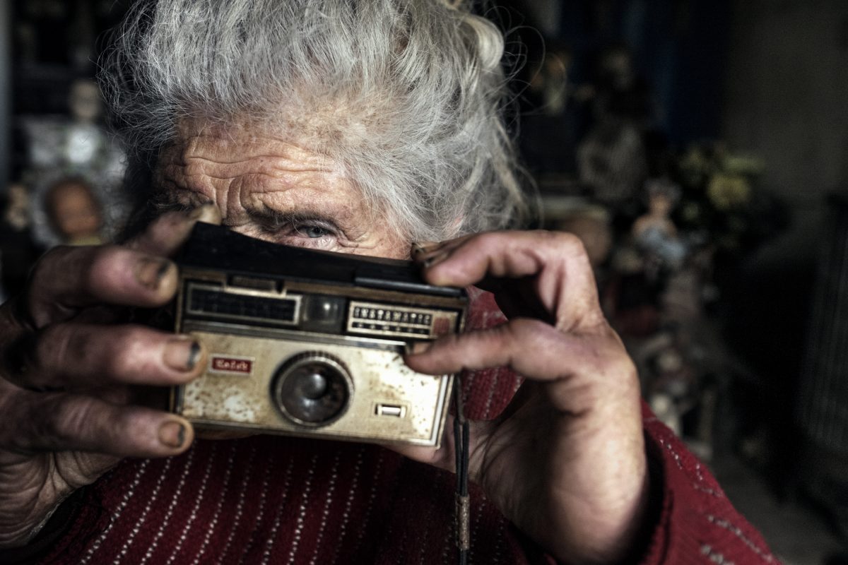 Dans le salon de Marie-Claude, au printemps. Elle a déterré un vieux Instamatic qu’elle a probablement chiné à une brocante. Il ne semble pas avoir servi récemment, malgré tout, elle invente plein d’histoires de photographies qu’elle aurait prises. / Extrait de « Marie-Claude, la dame aux poupées », © Mélanie Wenger